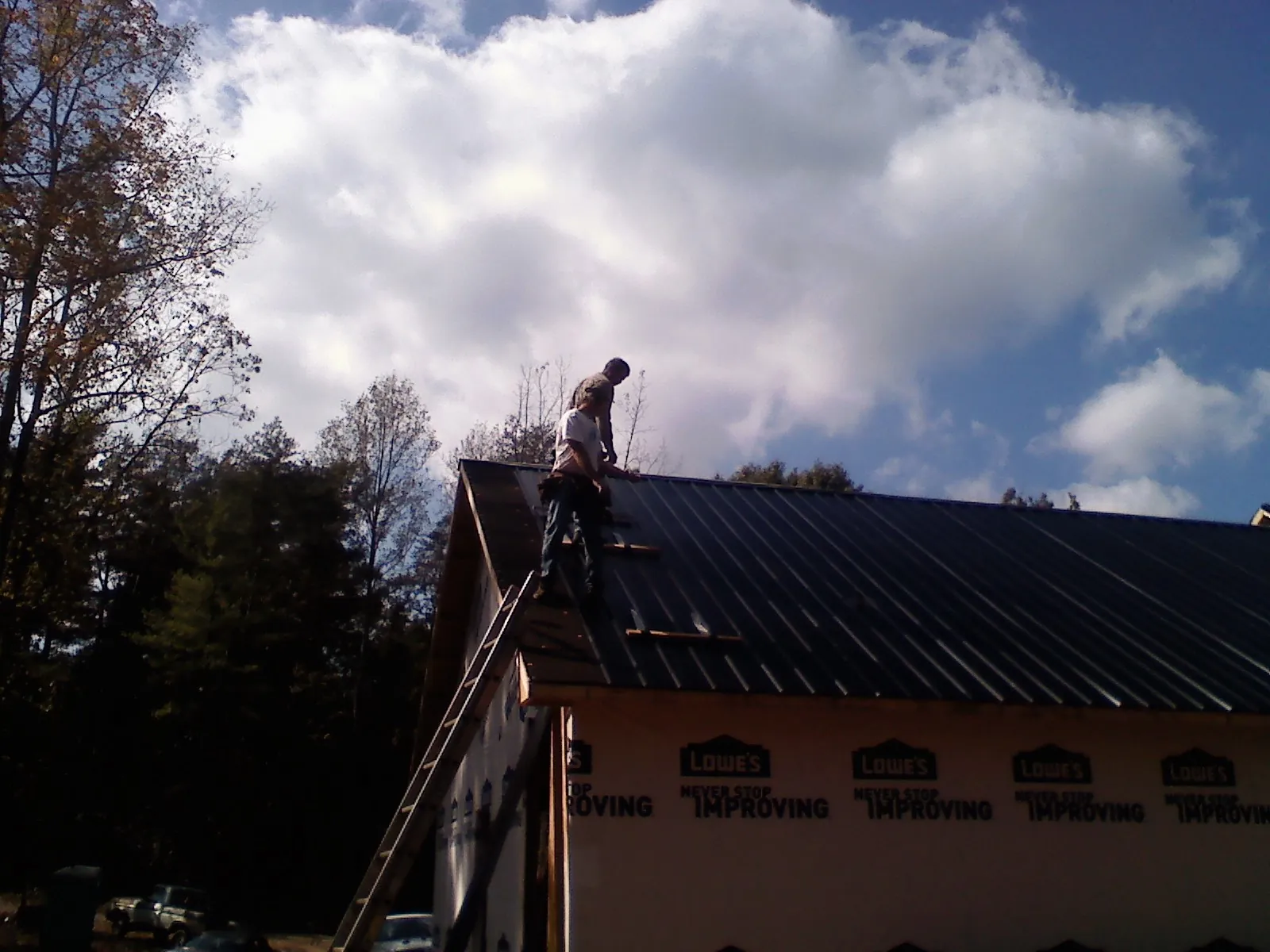 Roofer fastening dark metal panels high against a cloudy sky, from a Roof Inspection job in Florence